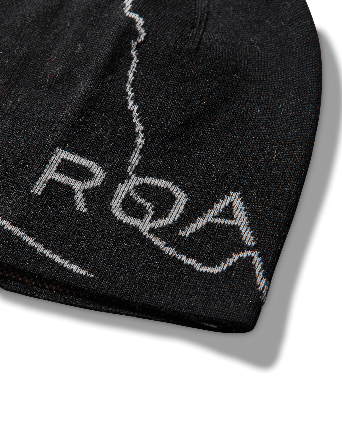 Close-up detail of the black beanie showing the light contrast line pattern and the embroidered “ROA” logo.