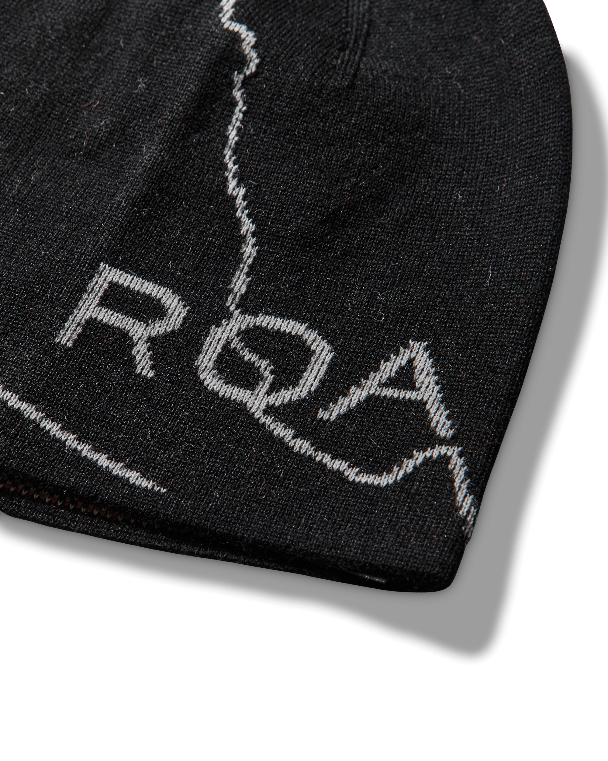 Close-up detail of the black beanie showing the light contrast line pattern and the embroidered “ROA” logo.