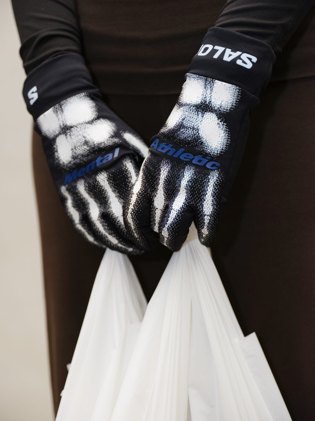 Mental Athletic BURNT KNUCKLES GLOVES worn while holding bag, black trail gloves with skeleton graphic design and Salomon branding