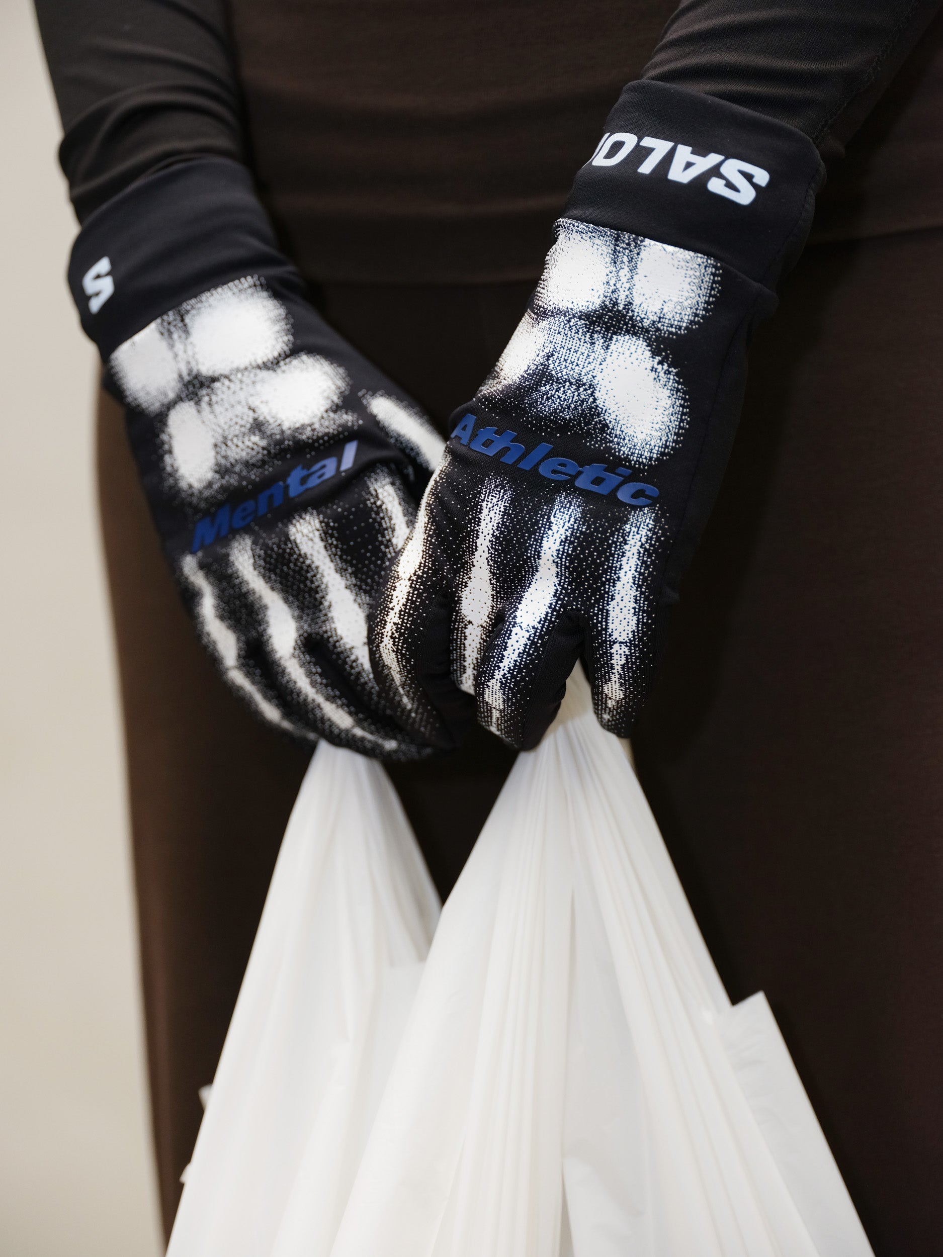 Mental Athletic BURNT KNUCKLES GLOVES worn while holding bag, black trail gloves with skeleton graphic design and Salomon branding